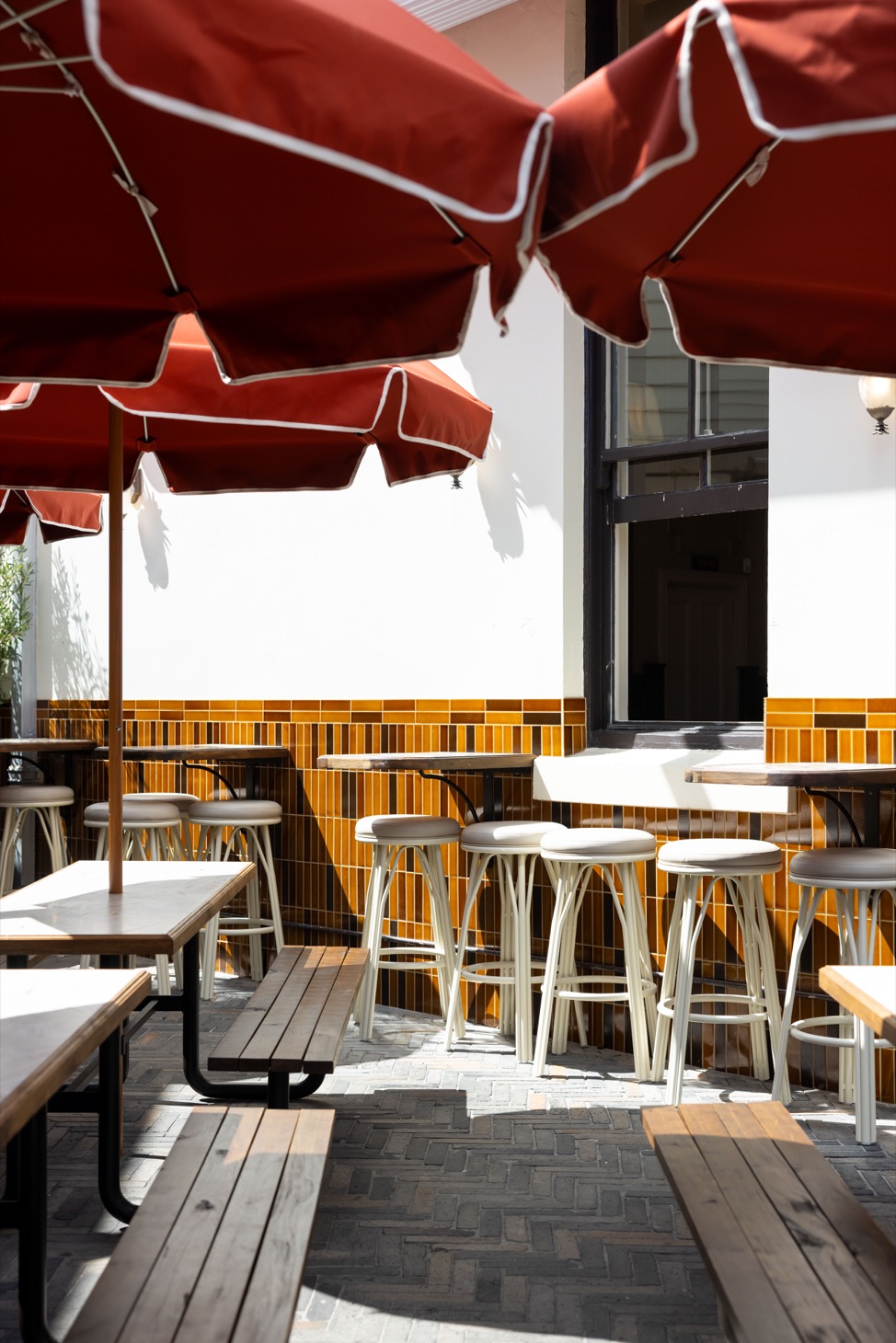Red umbrellas, timber benches and stools in the beer garden